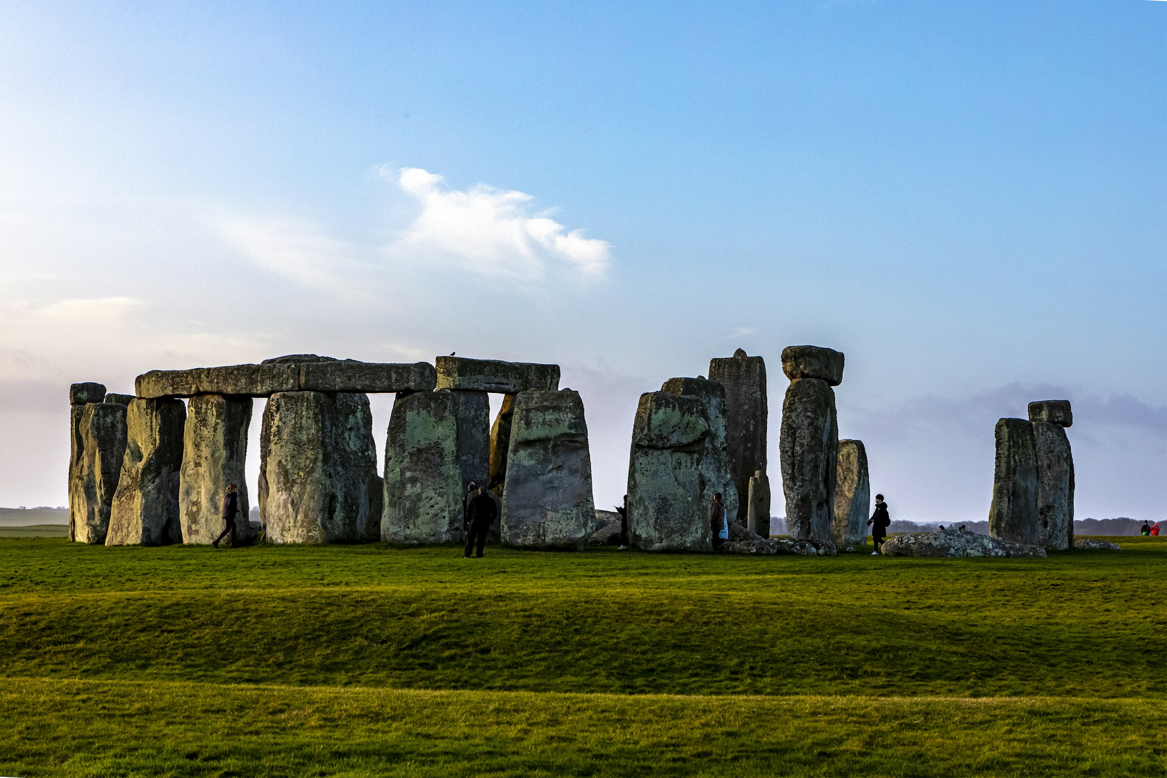 Stonehenge's stone circle under a bright, clouded sky, low light catching the grass